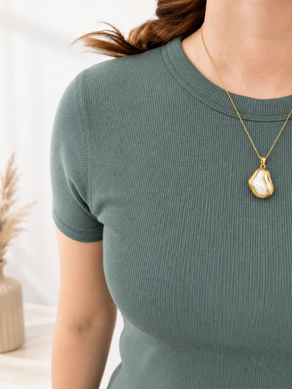 Person wearing a green ribbed shirt with a gold necklace featuring a large pendant.