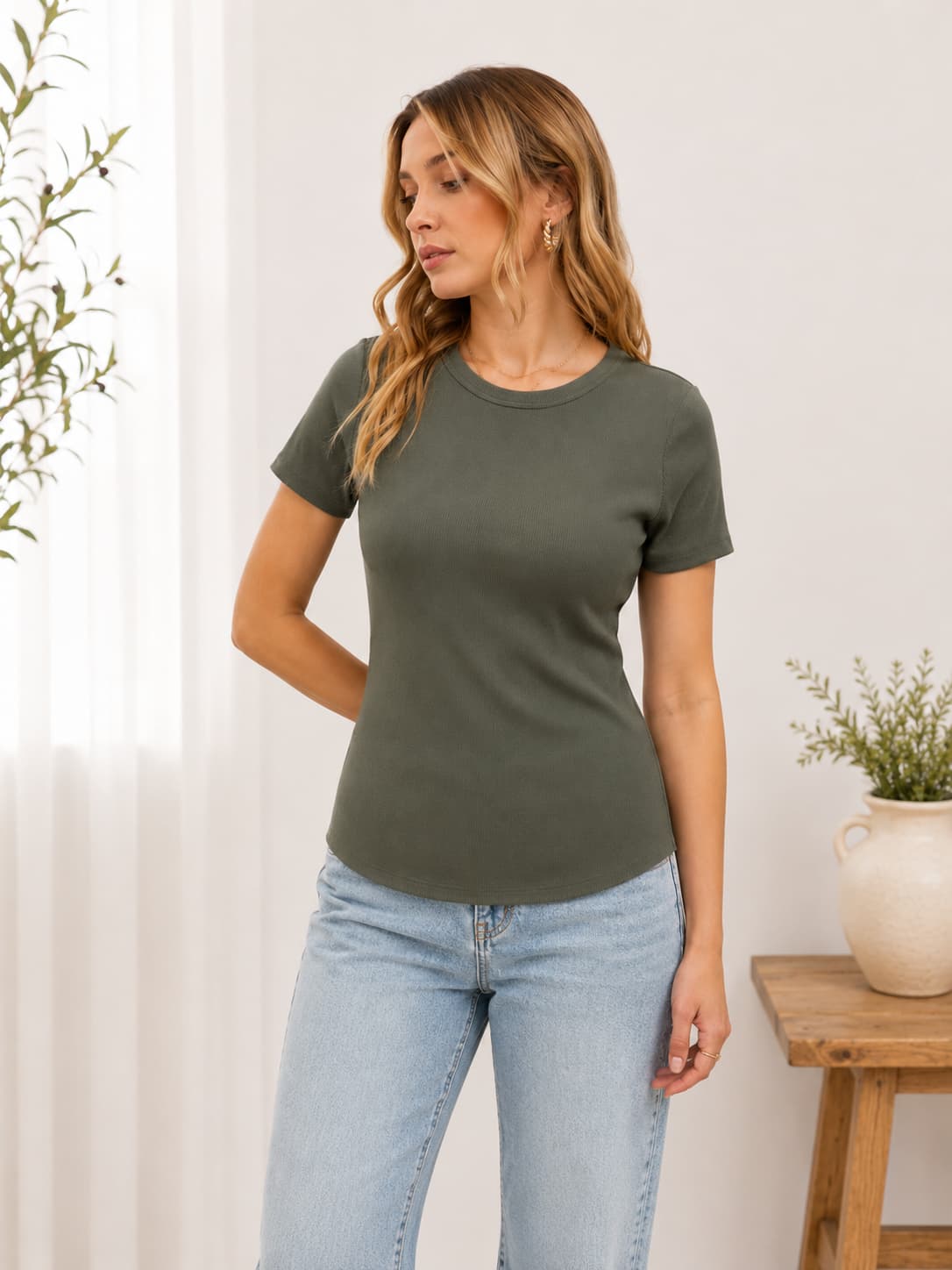 Woman wearing a green t-shirt and light blue jeans in a minimalistic room.