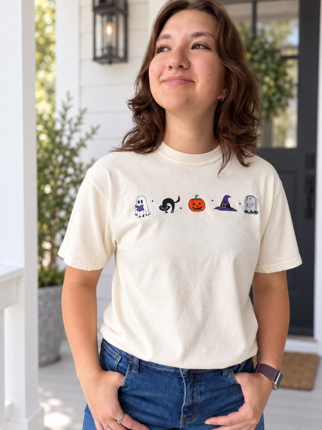 woman in cream colored tee shirt with halloween icons across the chest.