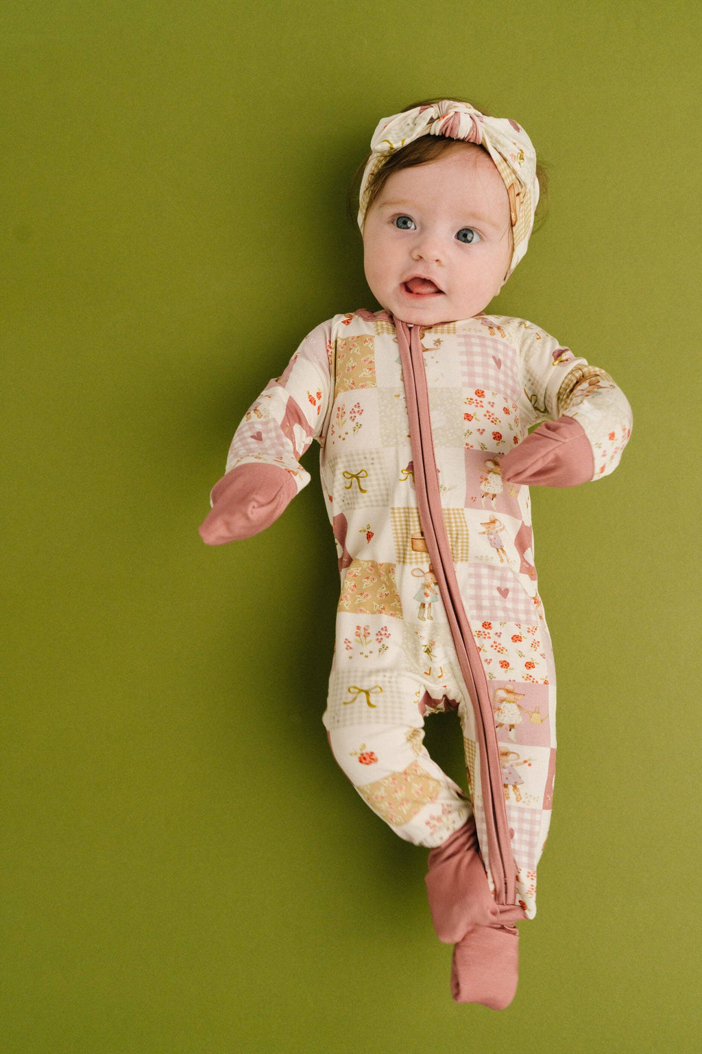 Baby in a patterned onesie and headband against a green background