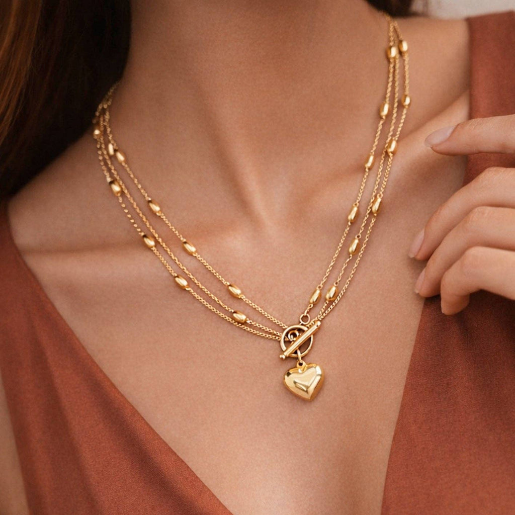 Gold necklace with heart pendant on a person wearing a rust-colored top.