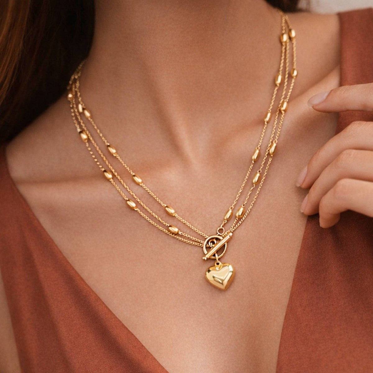 Gold necklace with heart pendant on a person wearing a rust-colored top.
