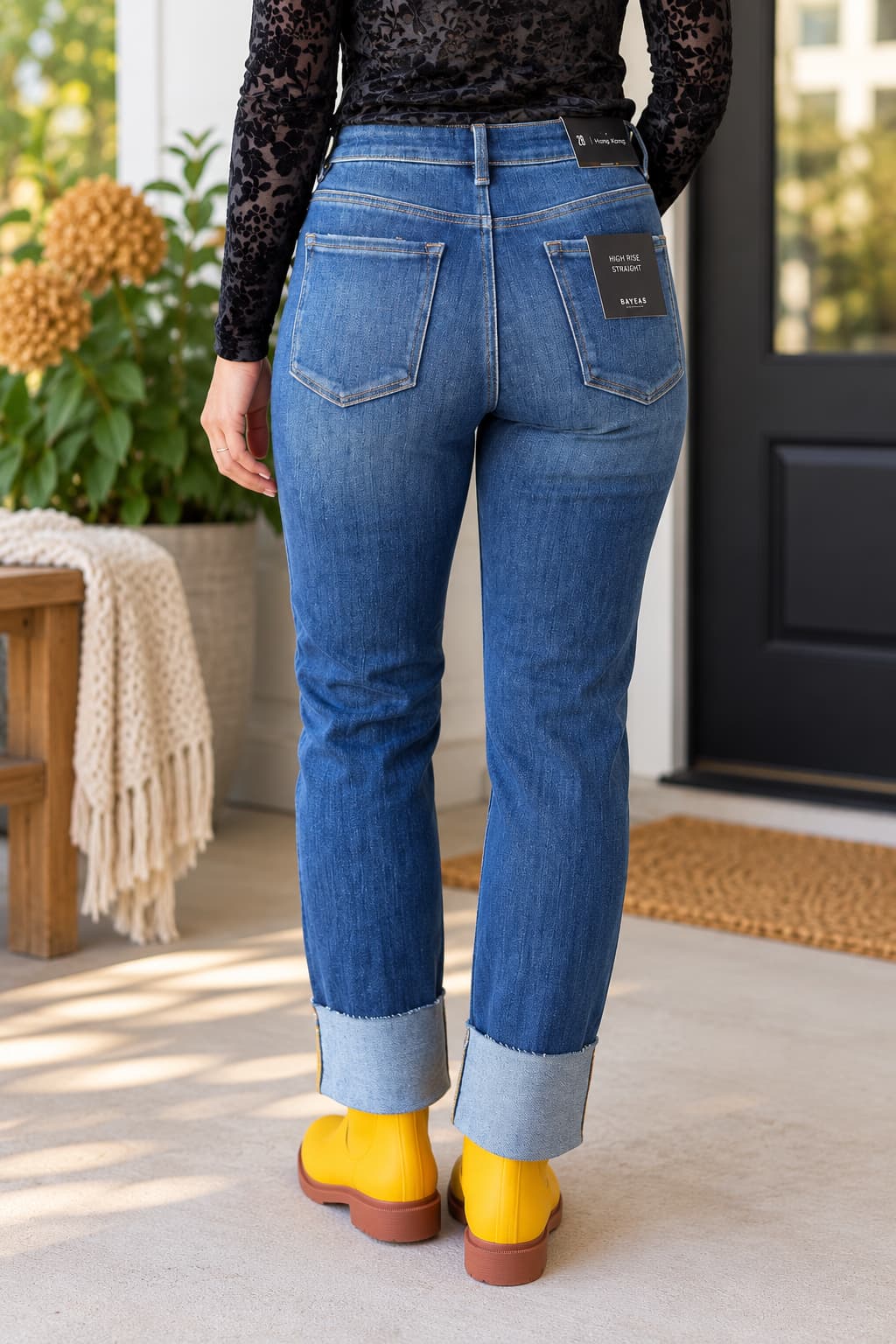 A person shown from the back wearing blue denim jeans with rolled cuffs, a black lace long-sleeve top, and bright yellow boots, standing on a porch in front of a black door.