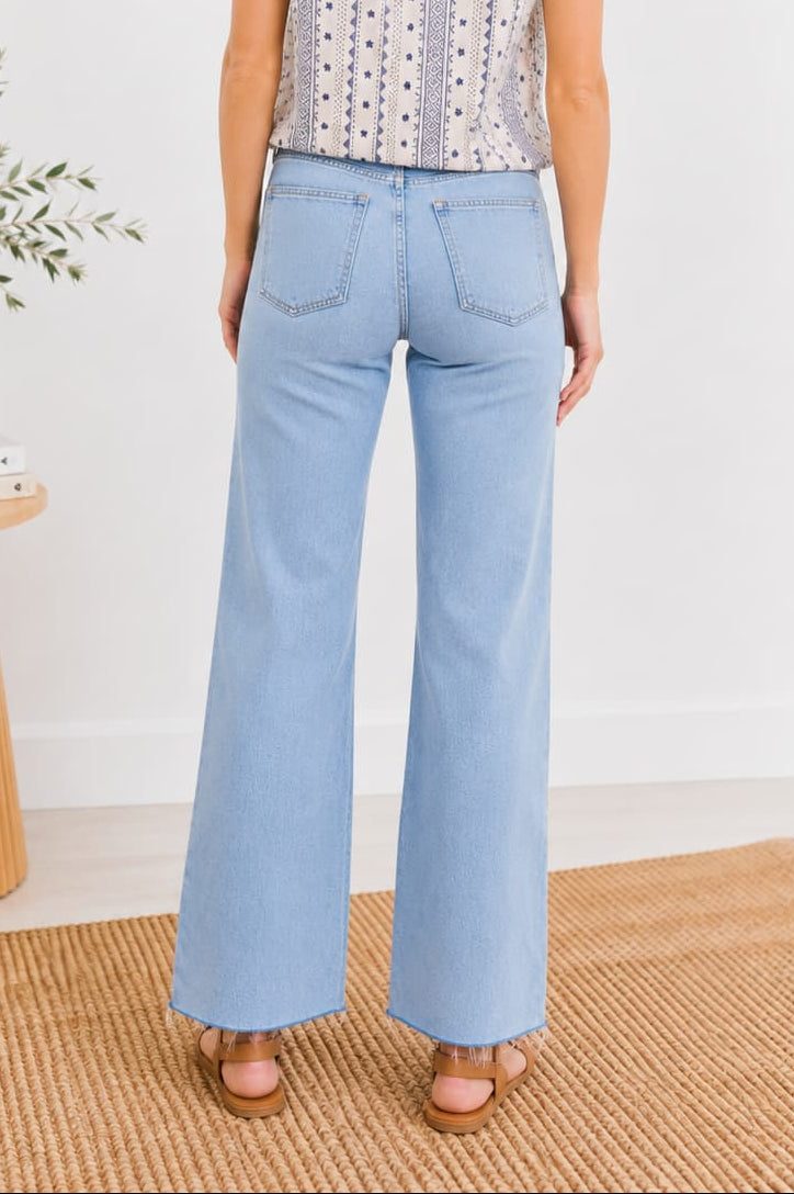 Woman wearing light blue jeans and a patterned top standing in a minimalistic room.