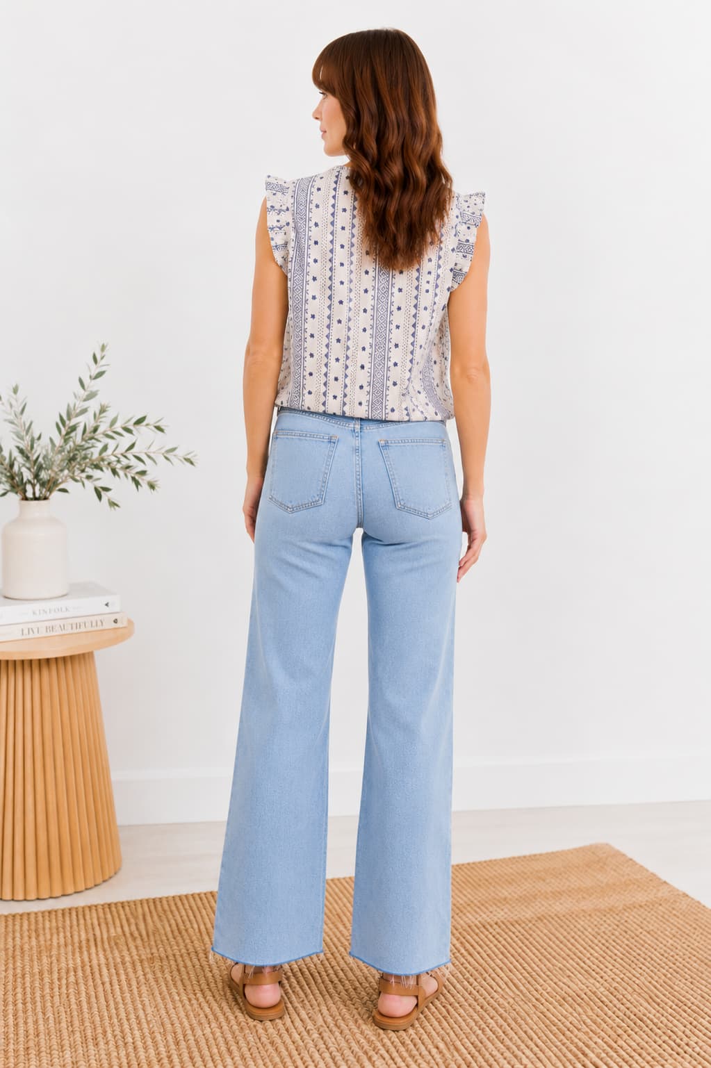 Woman wearing light blue jeans and a patterned top standing in a minimalistic room.