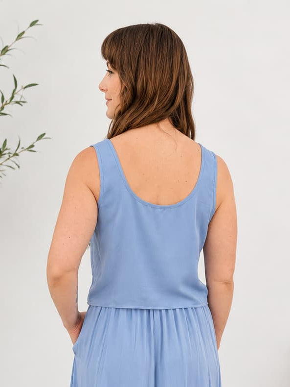 Woman wearing a blue crop top standing in a room with a plant and wooden bench.