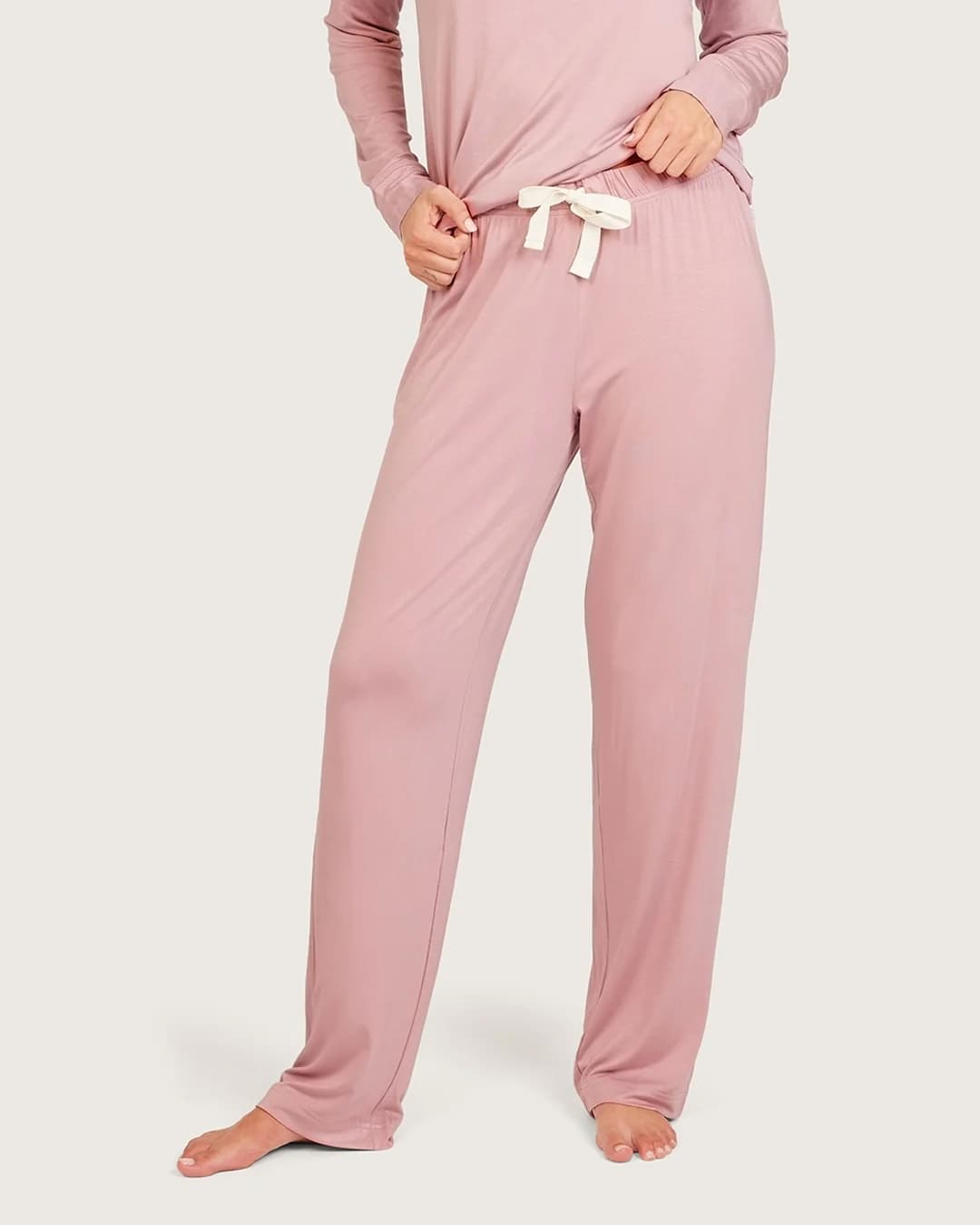 A person wearing dusty lilac lounge pants with a white drawstring and a matching long-sleeve top, shown against a plain light gray studio background.