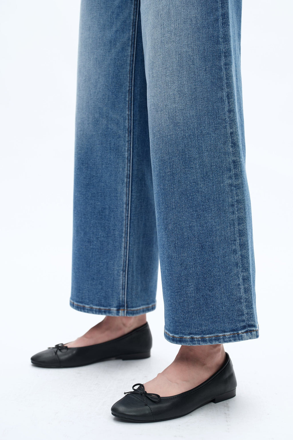 Person wearing blue jeans and black flats on a white background