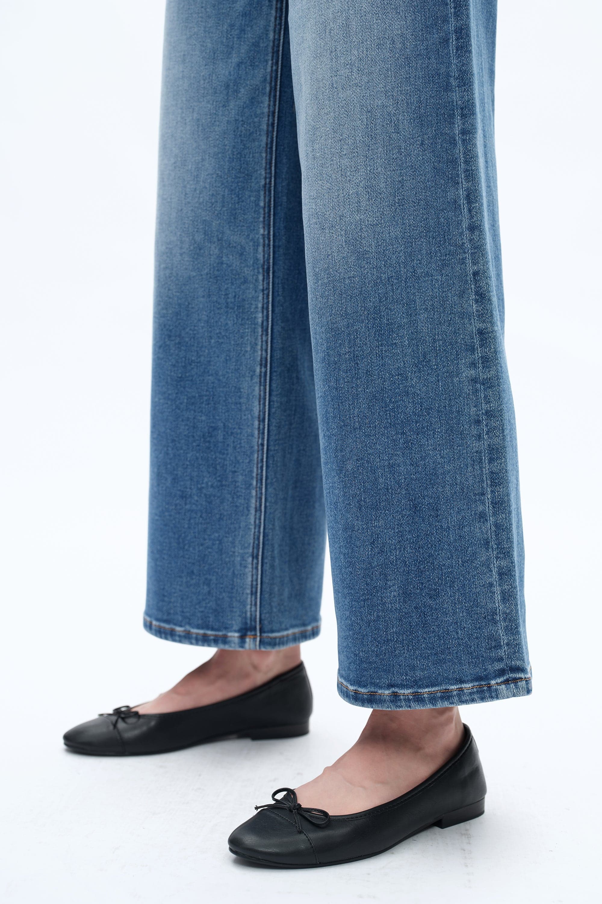 Person wearing blue jeans and black flats on a white background