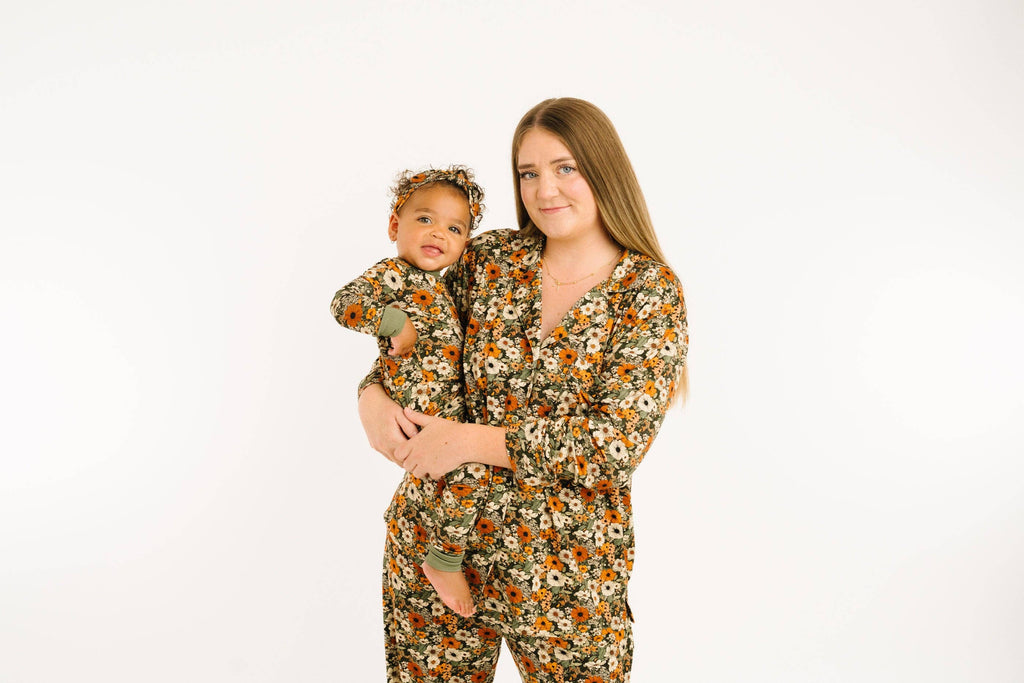 A woman holding a baby, both wearing matching floral print long-sleeve pajamas and a matching headband, against a plain white background.