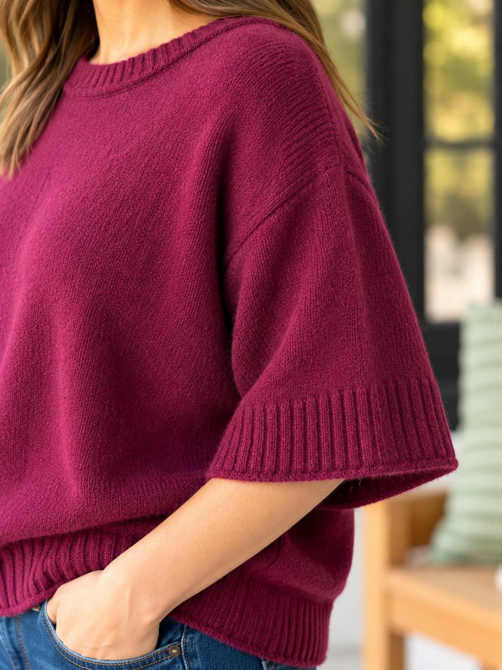 A close-up of a woman wearing a short-sleeve knit sweater in deep burgundy with ribbed trim, paired with blue jeans.