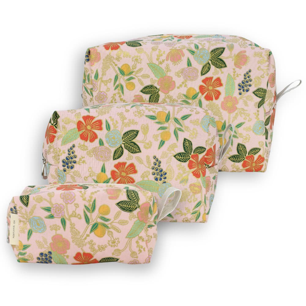 Three matching zippered cosmetic pouches in a soft pink floral print, arranged in a nested stack on a white background.