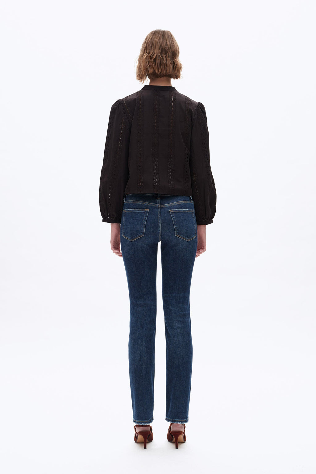 A model viewed from the back wearing a black long-sleeve blouse with puffed shoulders and dark blue skinny jeans, standing against a plain white background.