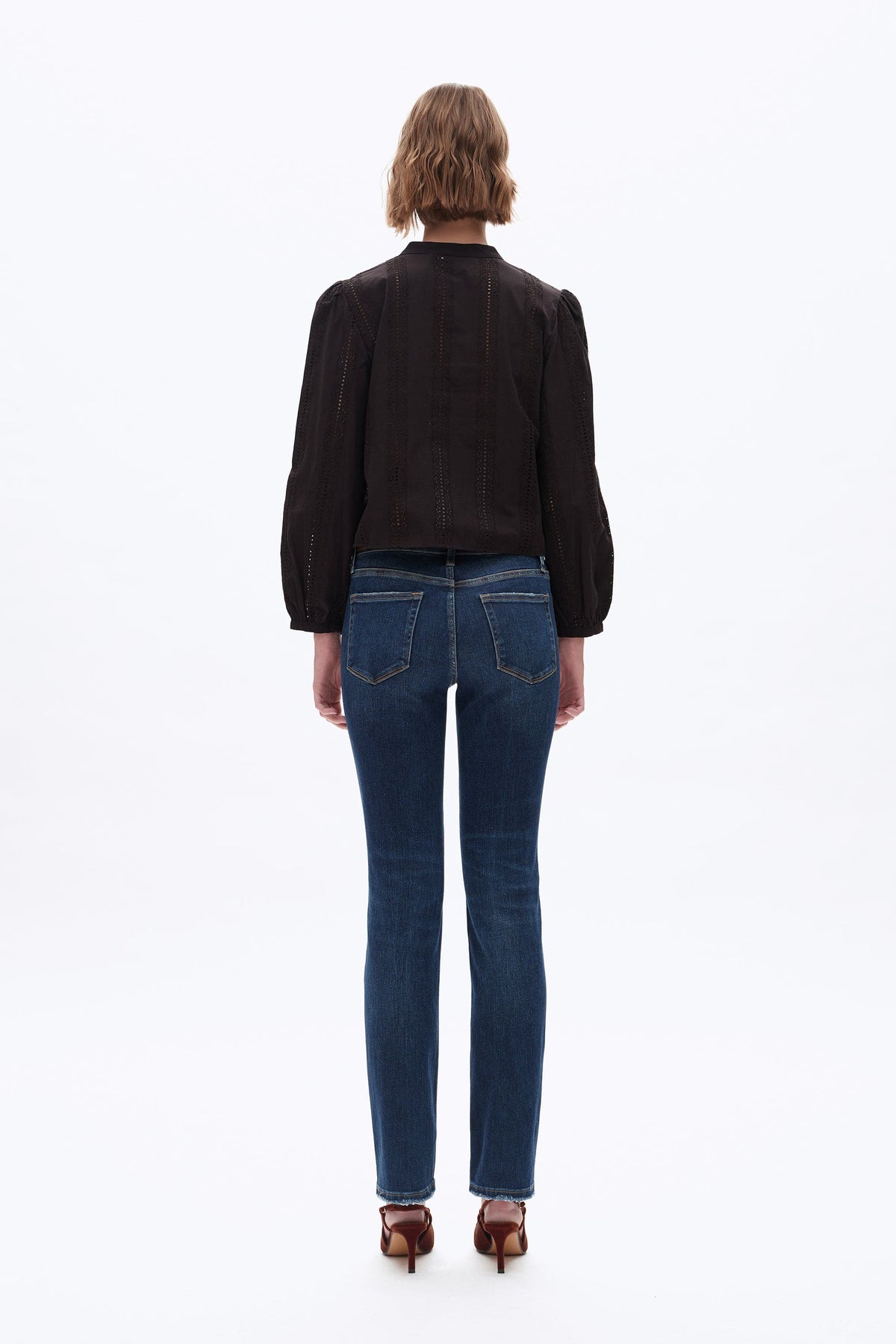 A model viewed from the back wearing a black long-sleeve blouse with puffed shoulders and dark blue skinny jeans, standing against a plain white background.