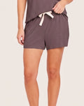 A person wearing dark taupe lounge shorts with a cream drawstring tie, shown from the waist down against a light beige studio background.