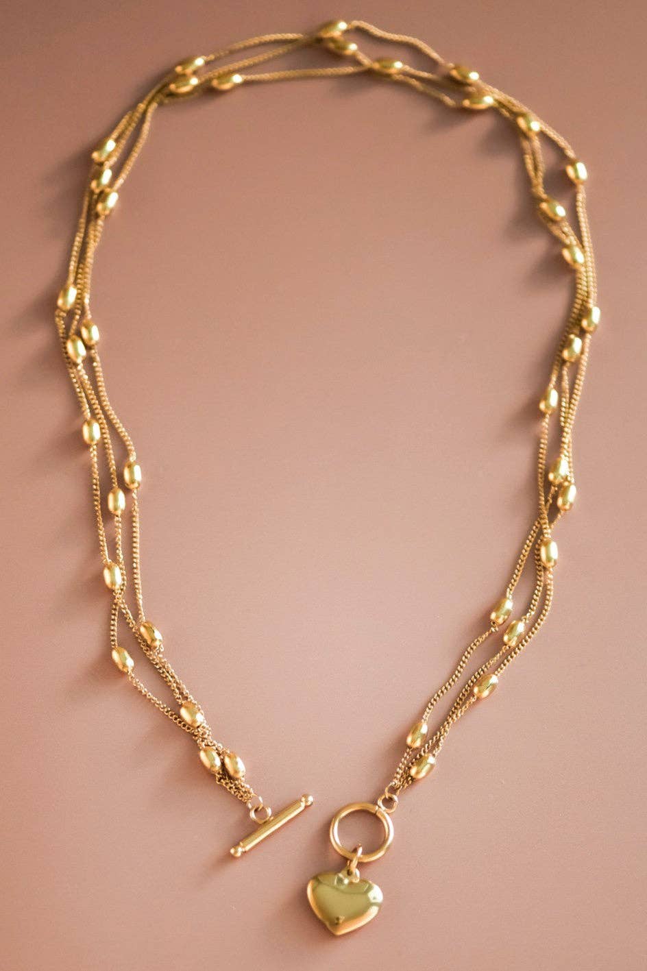 Gold necklace with heart pendant on a pink background