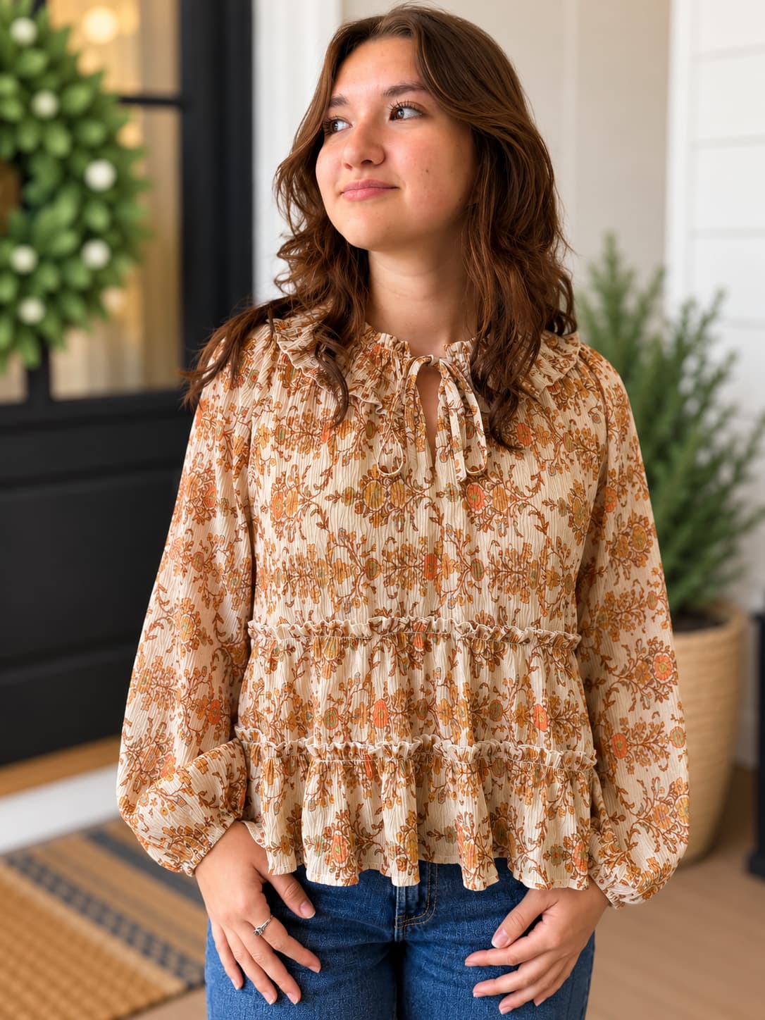 Woman wearing printed boho style peasant blouse top in beautiful orange and tan colors with blue denim.
