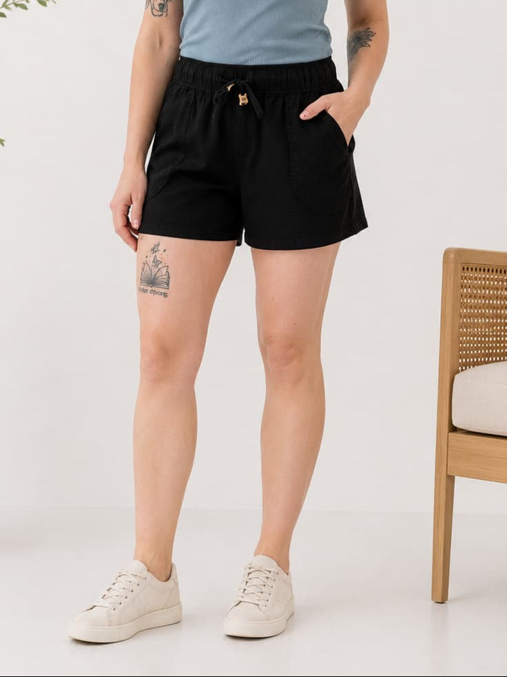 Woman wearing a blue t-shirt and black shorts standing in a minimalistic room.