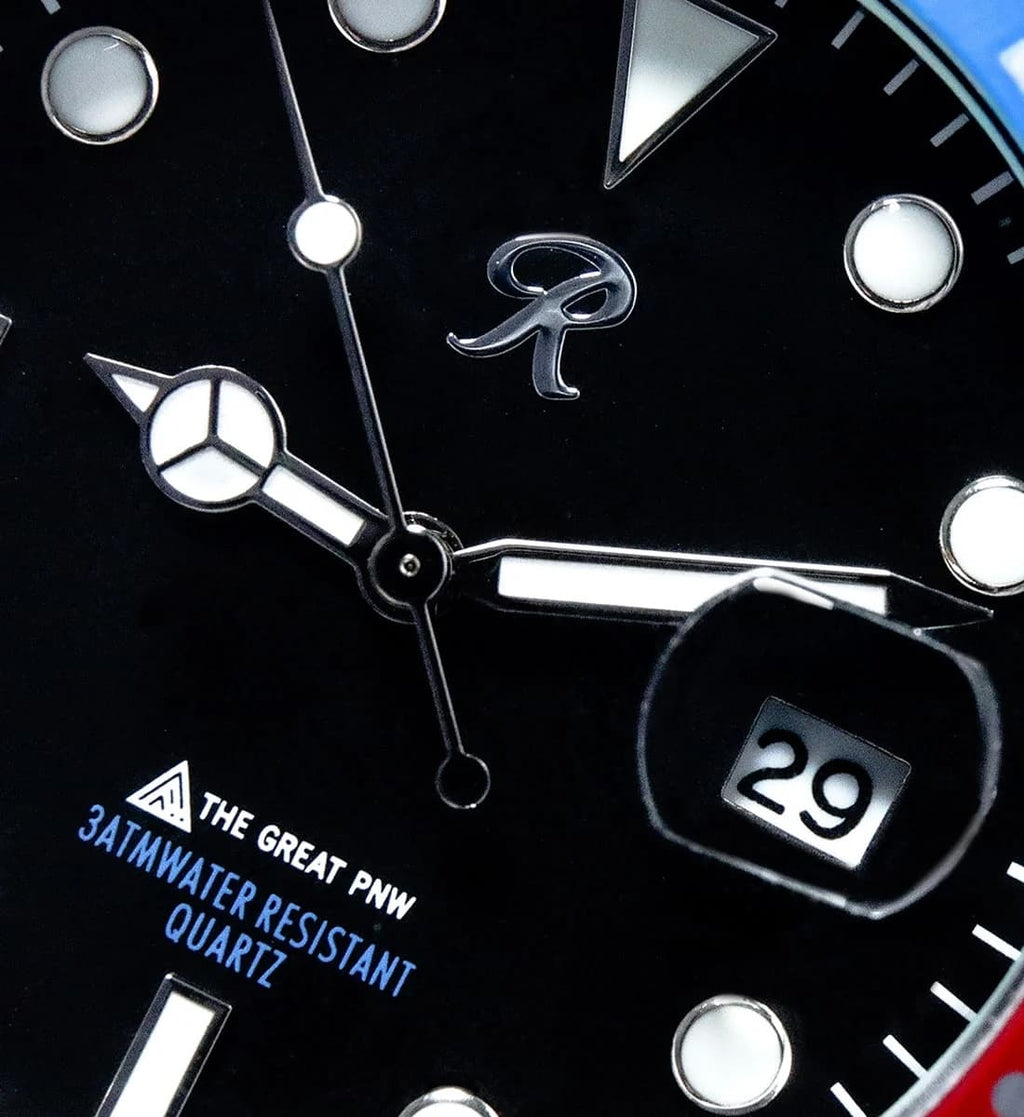 Close-up of a black watch dial with silver hands, luminous hour markers, a date window showing 29, and blue text reading 'THE GREAT PNW 3ATM WATER RESISTANT QUARTZ'.