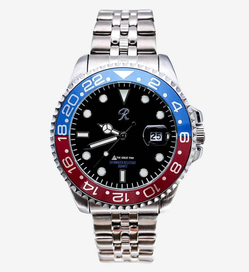 A stainless steel wristwatch with a black dial, a red and blue bezel, and a matching steel link bracelet, shown against a light gray background.