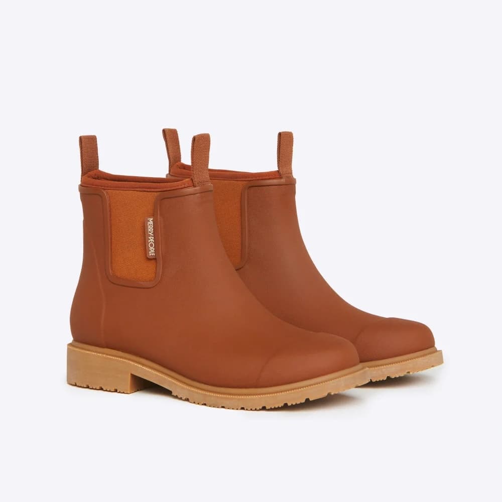 A pair of women's Chelsea-style ankle rain boots boots in a warm cognac brown, featuring elastic side panels and pull tabs, with a light tan block heel and sole, shown on a light gray background.