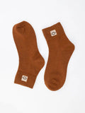 A pair of brown crew socks with small white embroidered smiley face patches on the cuffs, displayed on a clean white background.