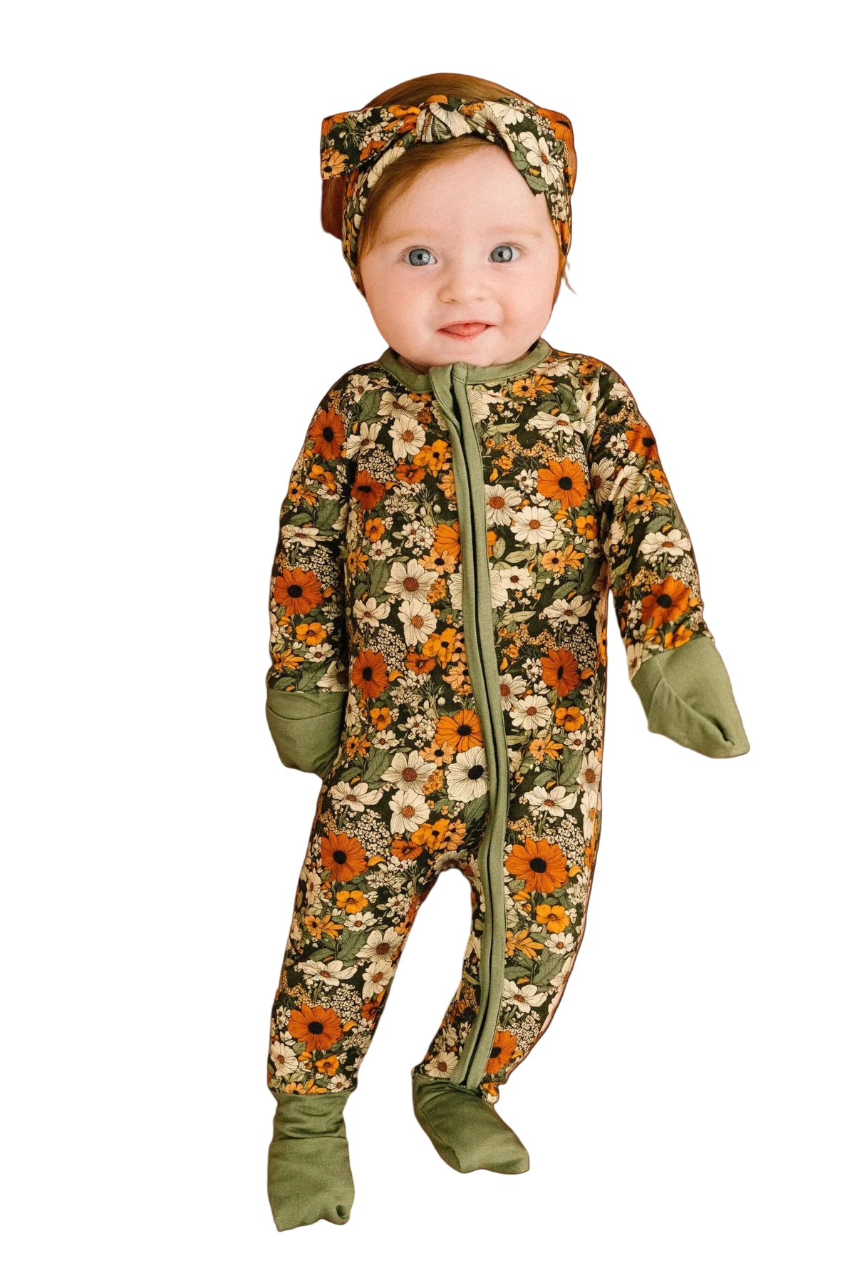 A baby wearing a floral print footed sleeper and matching headband, posed against a solid terracotta background.