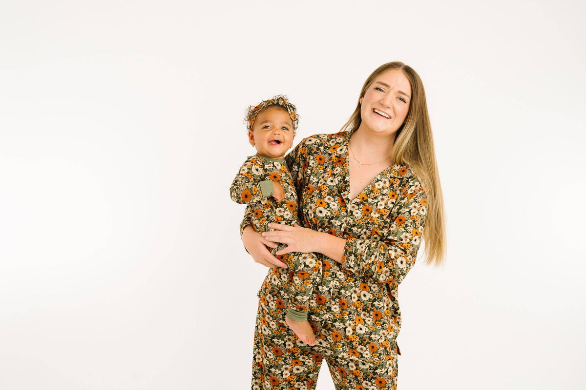 A woman holding a baby, both wearing matching floral print pajamas against a plain white studio background.