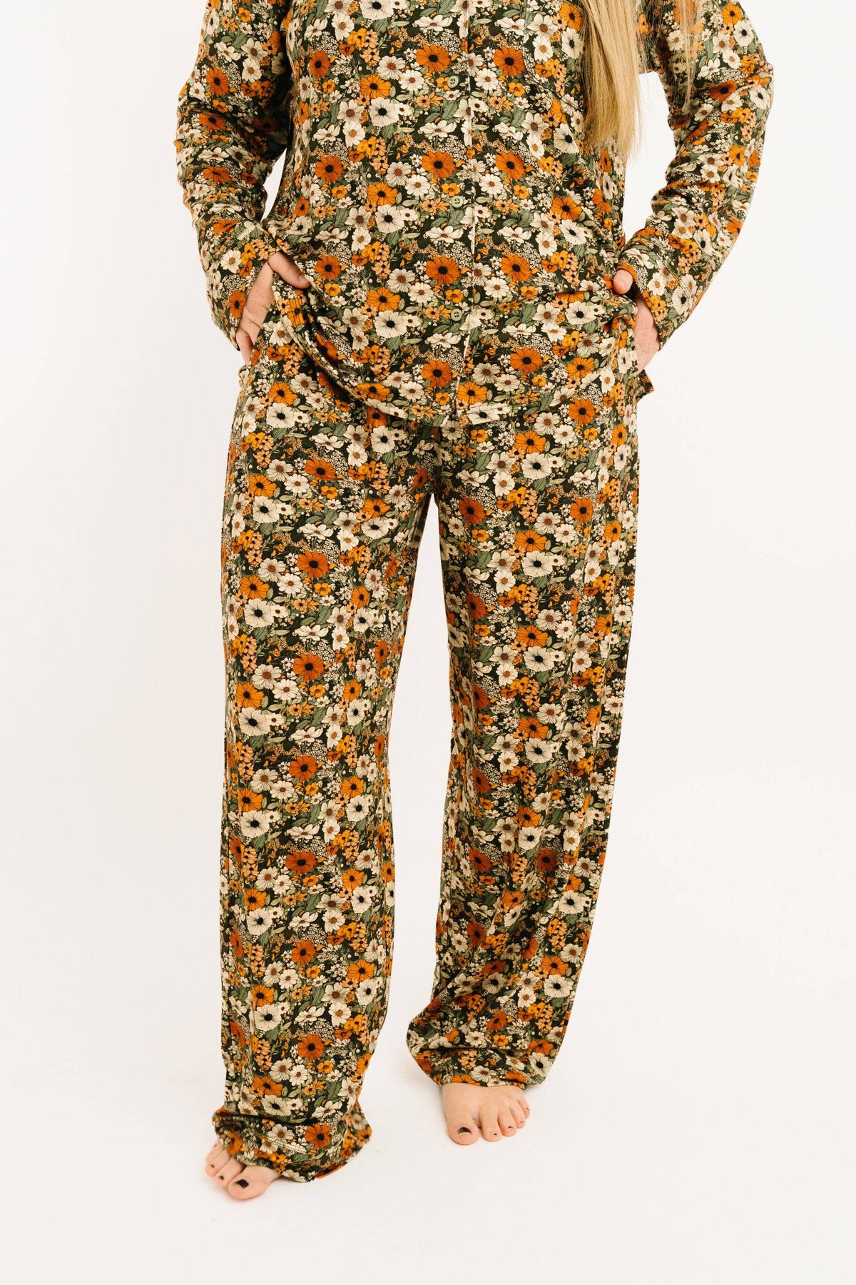 A person wearing a long-sleeve pajama set with an all-over floral print in orange, cream, and olive green, standing against a plain white background.