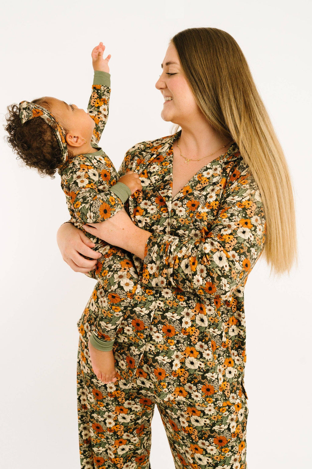 A woman and a baby wearing matching floral pajamas, with the woman holding the baby against a plain white background.