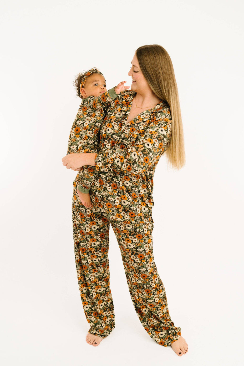 A woman and a baby wearing matching floral print pajamas, standing against a plain white studio background.