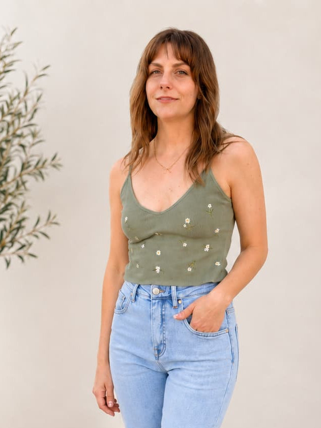 Woman wearing a green top with embroidered daisy flowers and light blue jeans