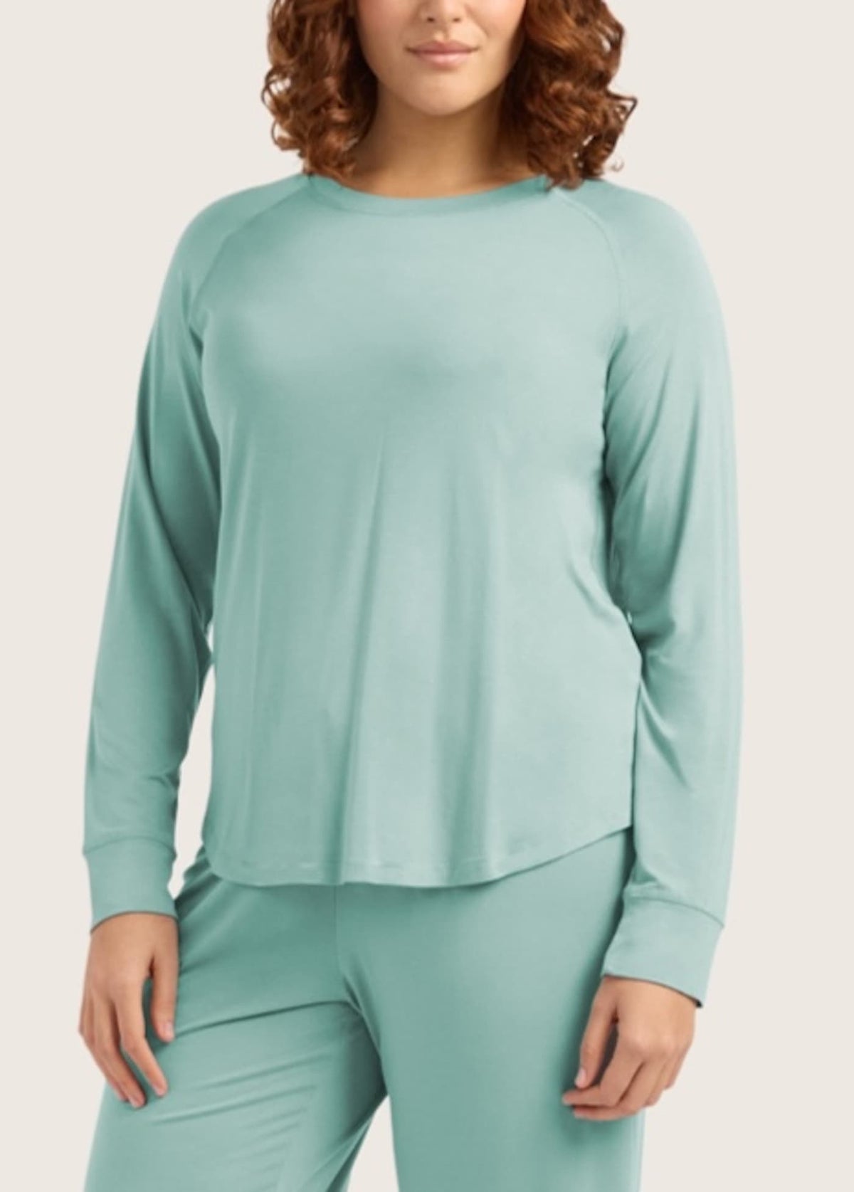 A woman wearing a matching two-piece loungewear set in a soft mint green color, featuring a long-sleeve top and coordinating pants, against a solid light beige background.