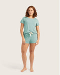 A woman modeling a two-piece mint green loungewear set consisting of a short-sleeve t-shirt and matching drawstring shorts, against a solid light beige background.