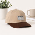 A beige and brown baseball cap with a white brand patch reading 'THE GREAT PWI Upper Lift, USA' on a clean white surface, styled with a potted plant and a mug in the background.