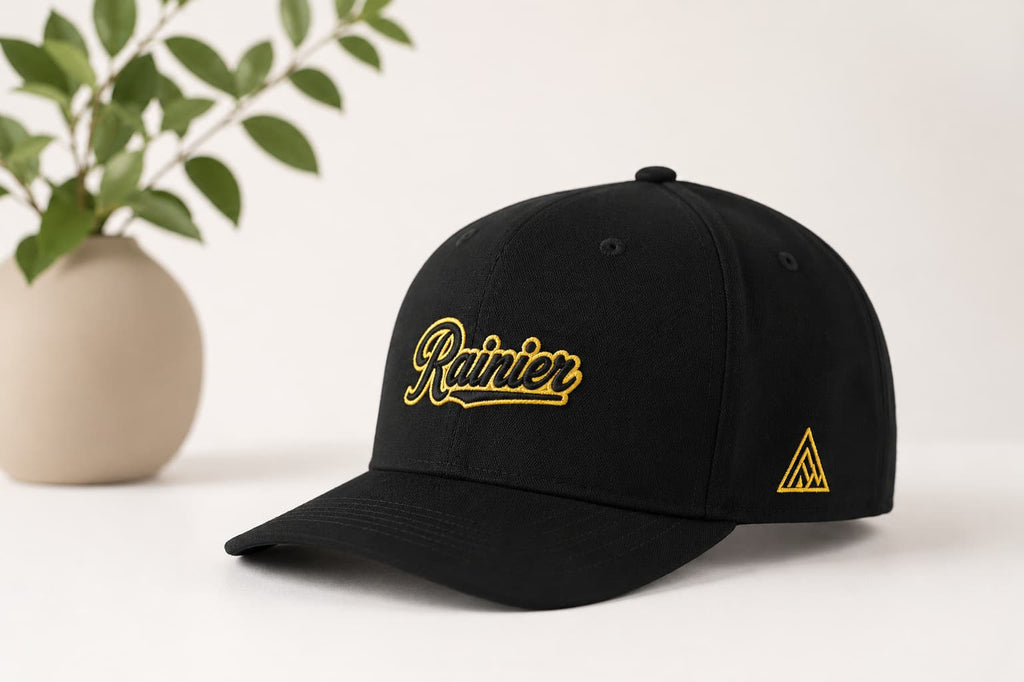 black snap back hat with Rainier logo embroidered in gold thread