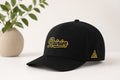 black snap back hat with Rainier logo embroidered in gold thread