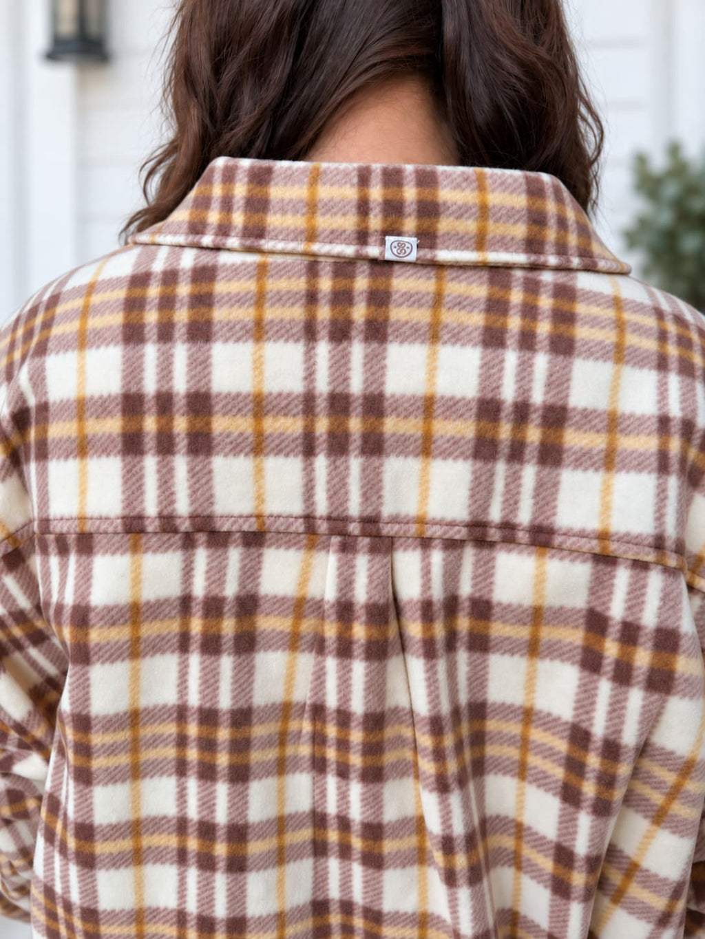 Close-up back view of a person wearing a plaid flannel shirt jacket in cream, brown, and mustard yellow.