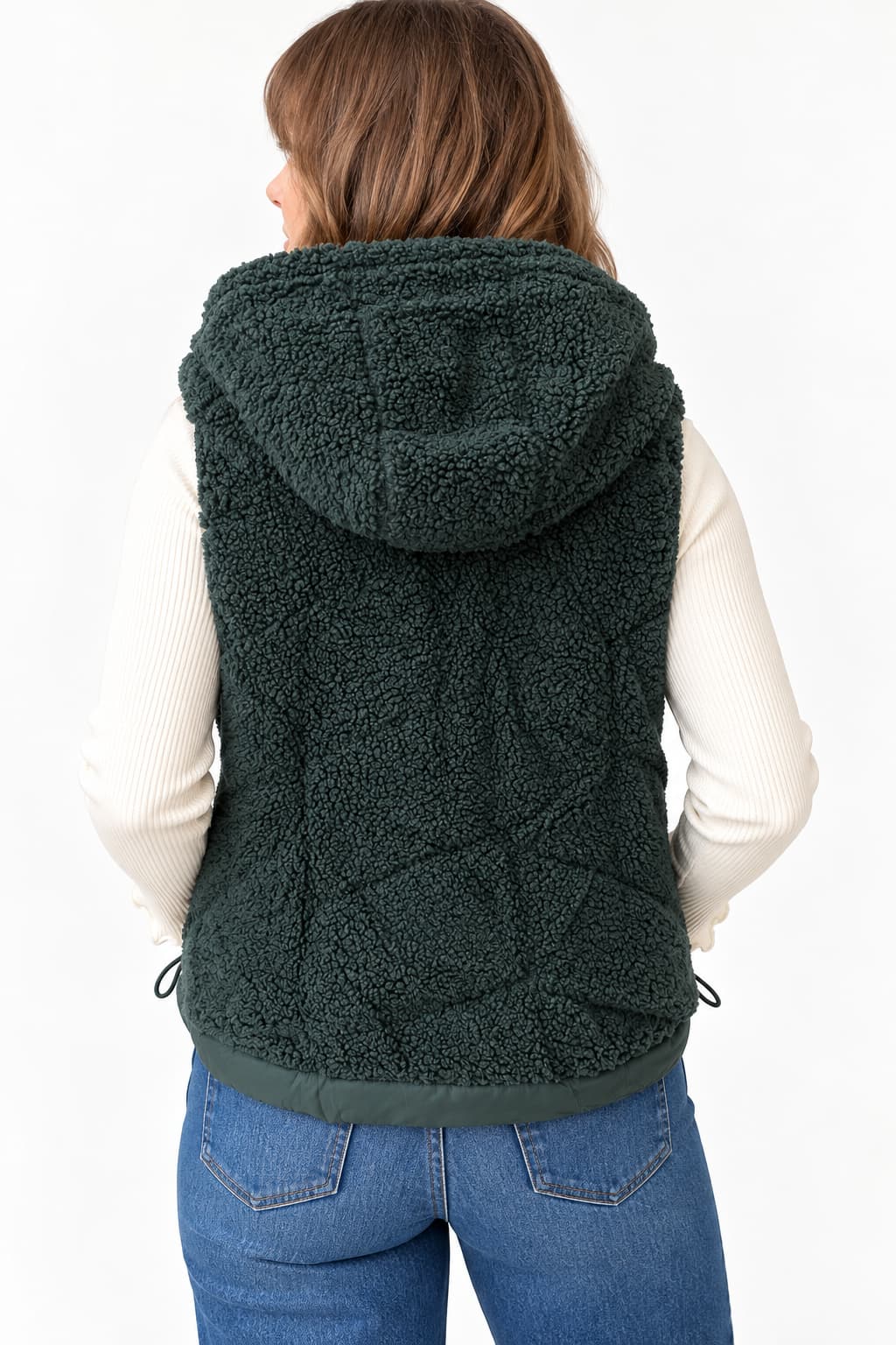 A woman viewed from the back wearing a dark forest green sherpa fleece hooded vest over a cream ribbed long-sleeve top and blue jeans, against a plain white studio background.