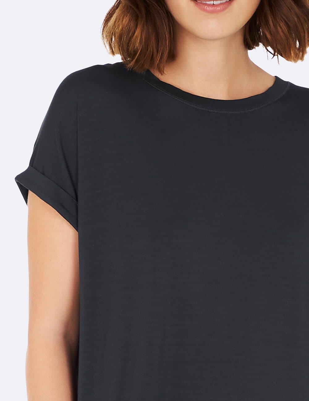 A close-up of a woman wearing a blue gray short-sleeve crewneck t-shirt with rolled cuffs, shown against a plain white background.