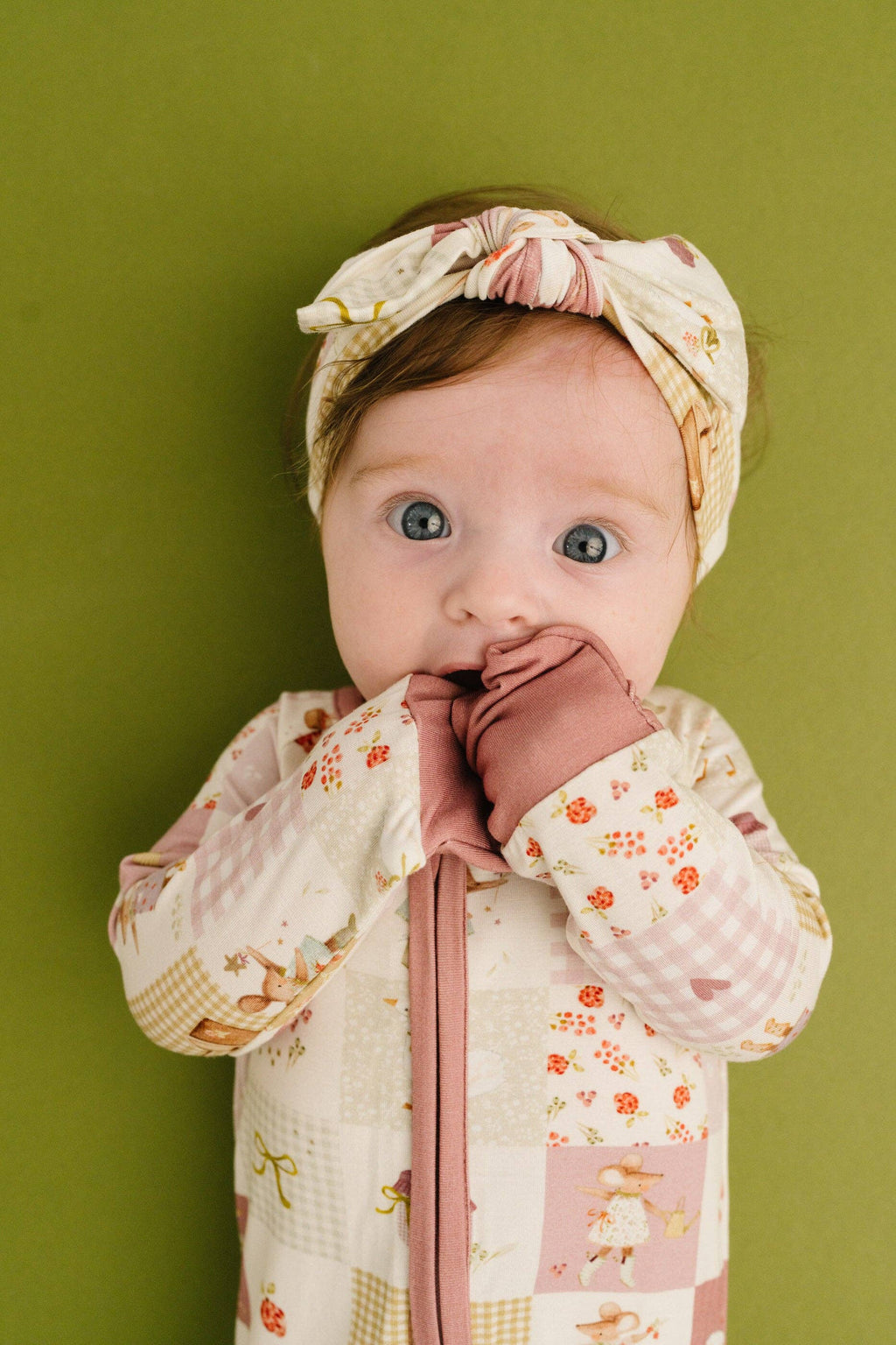 Baby wearing a floral headband and patterned outfit against a green background