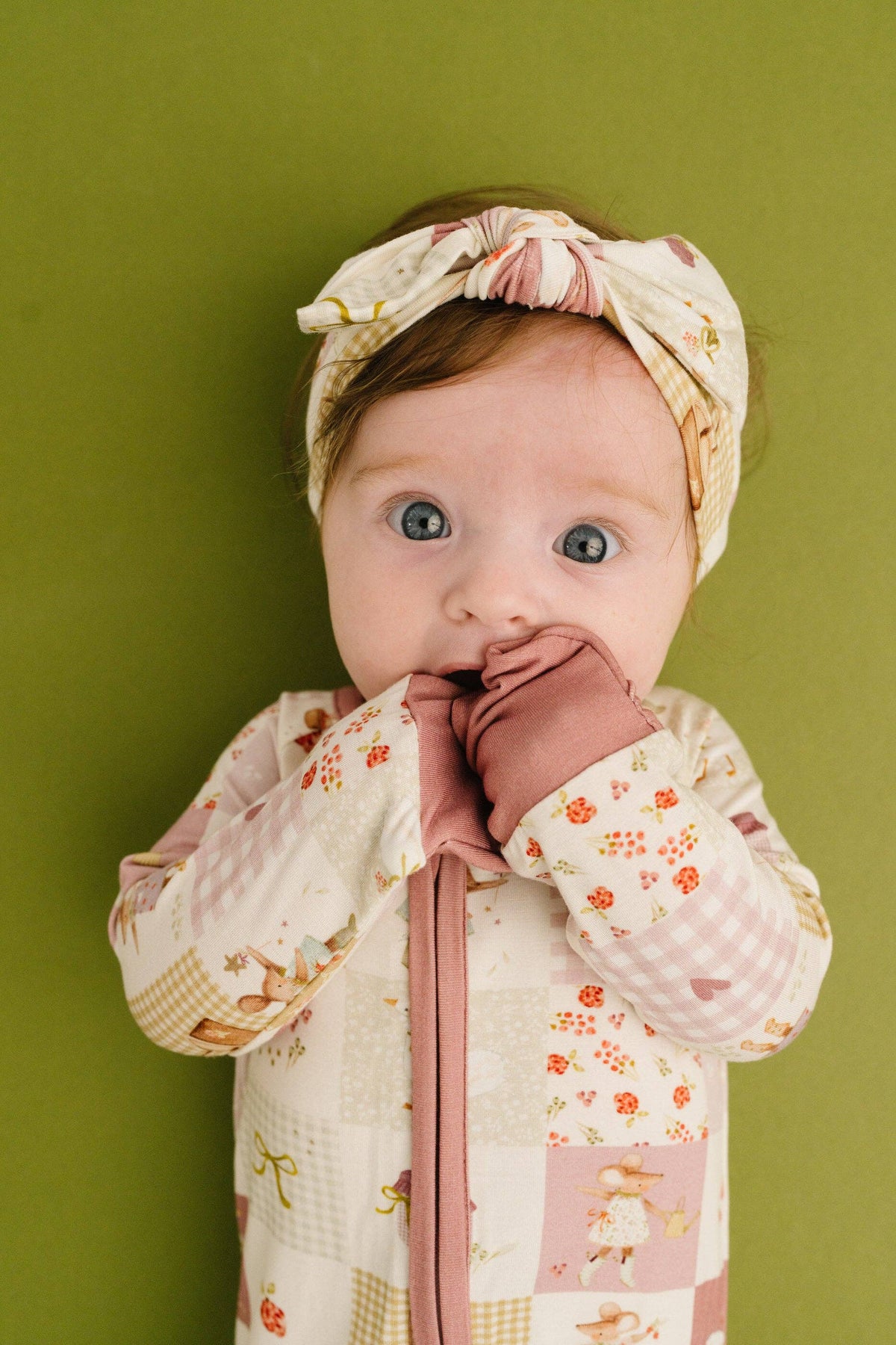 Baby wearing a floral headband and patterned outfit against a green background