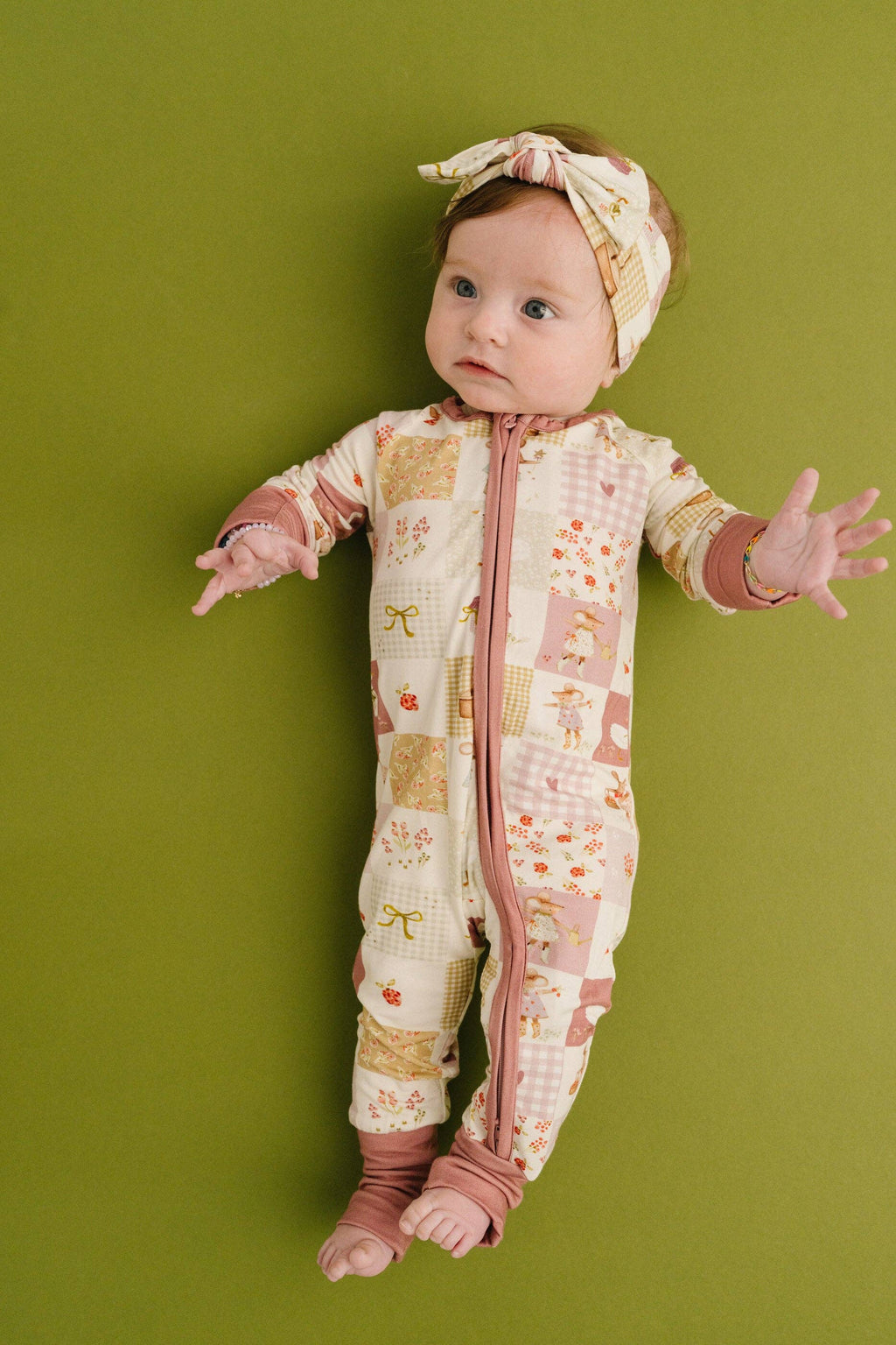 Baby in a patterned onesie with a headband on a green background