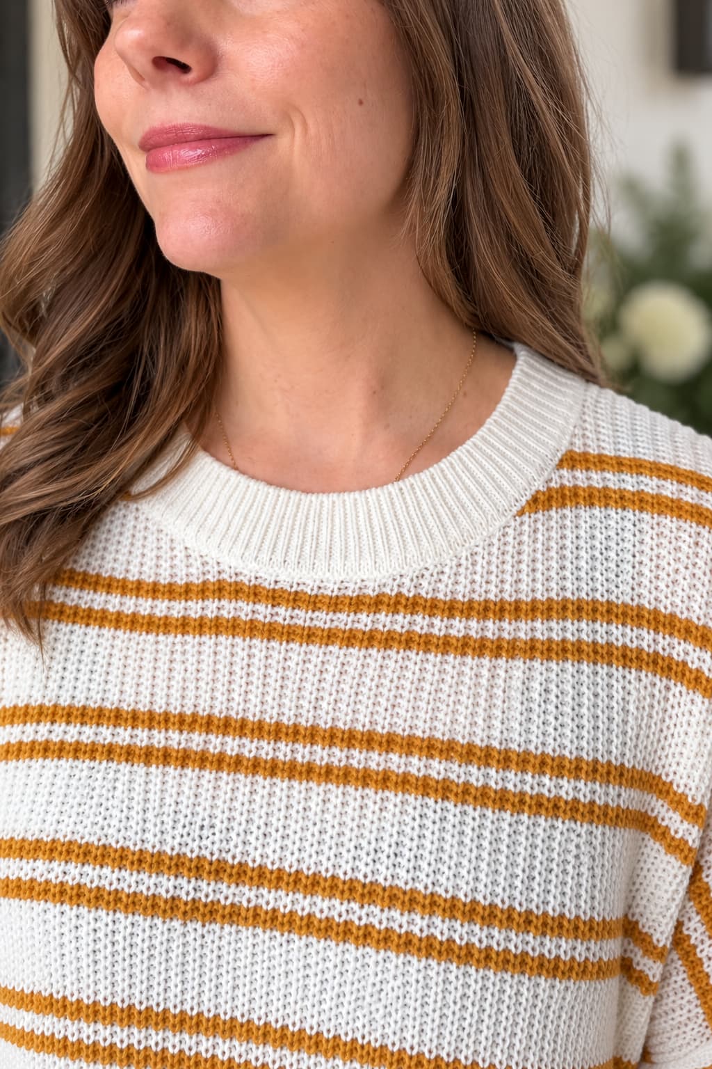 A close-up of a woman wearing a cream-colored knit sweater with horizontal mustard yellow stripes.
