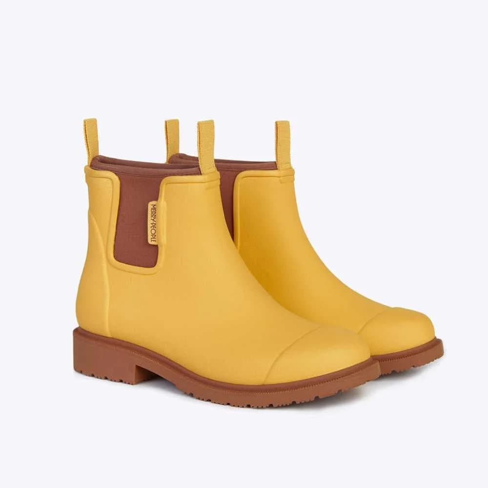 Pair of yellow rain boots with brown soles on a light gray background
