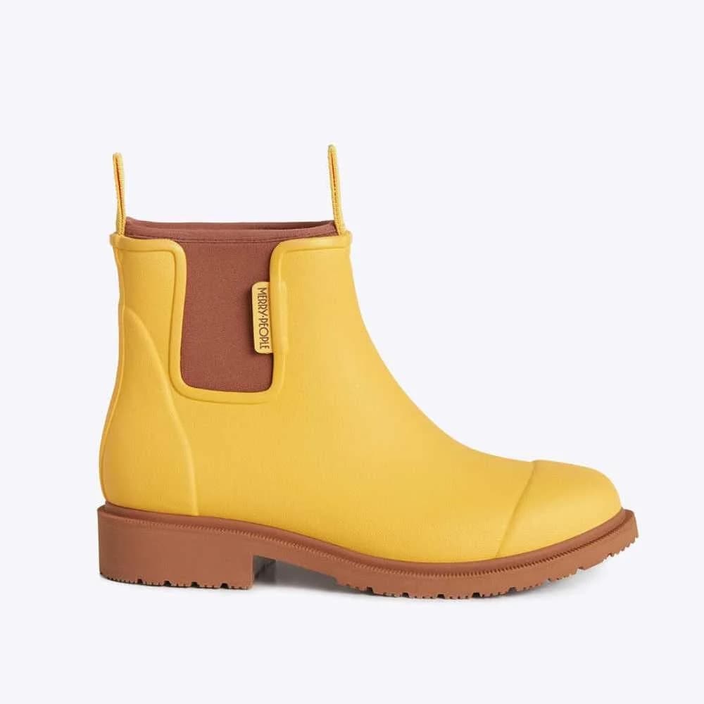 A single yellow rubber Chelsea boot with a brown elastic side panel, pull tabs, and a brown lug sole, shown from a side profile on a light gray background.