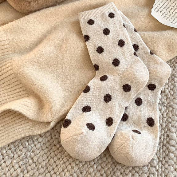Pair of beige socks with black polka dots on a textured surface with shoes and a plush toy.