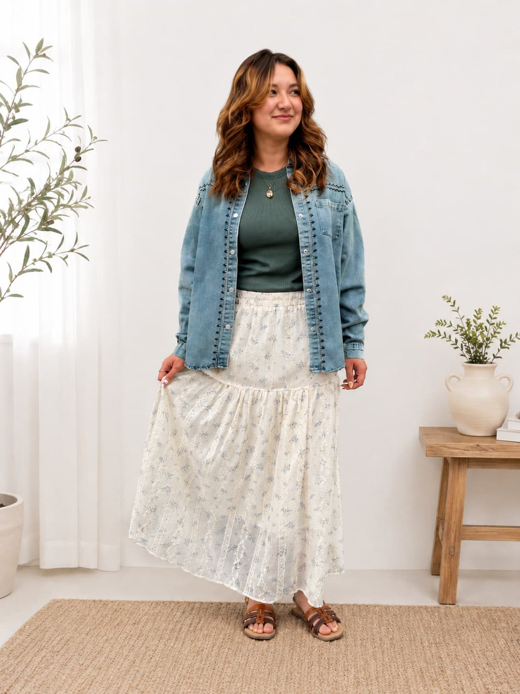 Woman wearing denim embroidered shirt jacket over a ribbed t shirt and tired floral maxi skirt in a home setting.