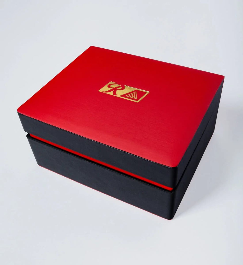 A square red and black gift box with a gold Raquel Welch logo on the lid, photographed on a light gray background.