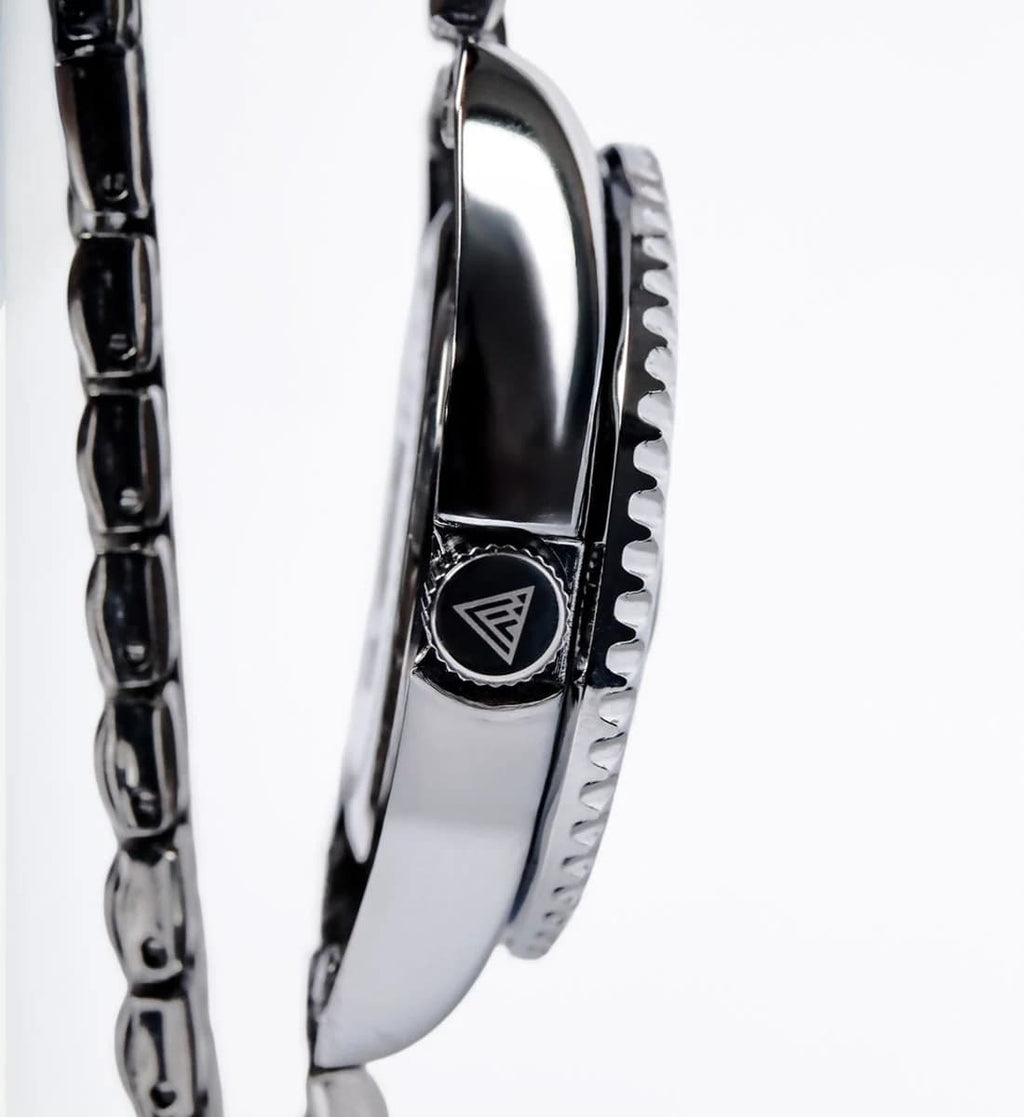 Close-up of a silver-toned metal watch with a textured bezel and a circular logo emblem on the side, shown against a white background.